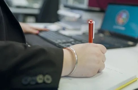 Person taking notes on paper with a laptop next to them