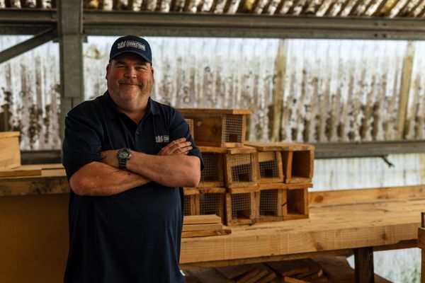 Community Work Supervisor stands smiling in workshop with rows of wooden boxes behind him